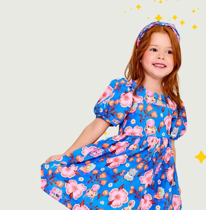 A imagem mostra uma menina ruiva com vestido estampado com fundo azul sobre um fundo neutro com estrelinhas amarelas.