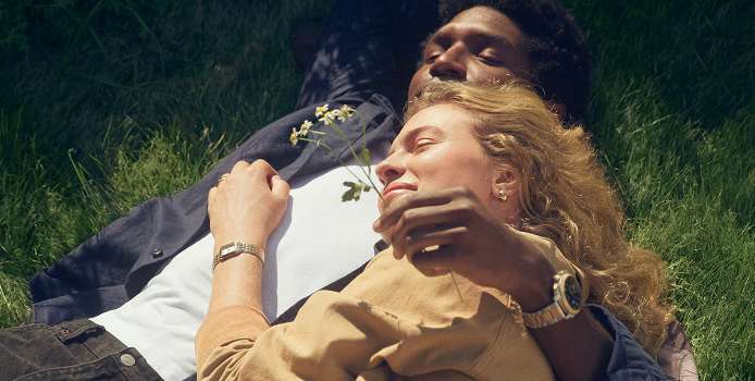 A couple lounging in the grass, each wearing Fossil watches.