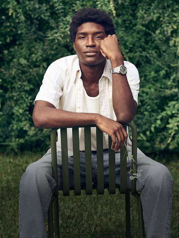 A man sitting in a chair in a spring meadow, wearing the Fossil Everett chronograph watch.