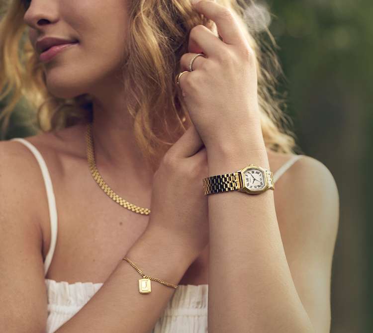 Interlocking chain bracelets with an engravable heart or name plate shown over a polaroid picture of a couple embracing. Illustrated yellow hearts add a Valentine's Day flourish.
