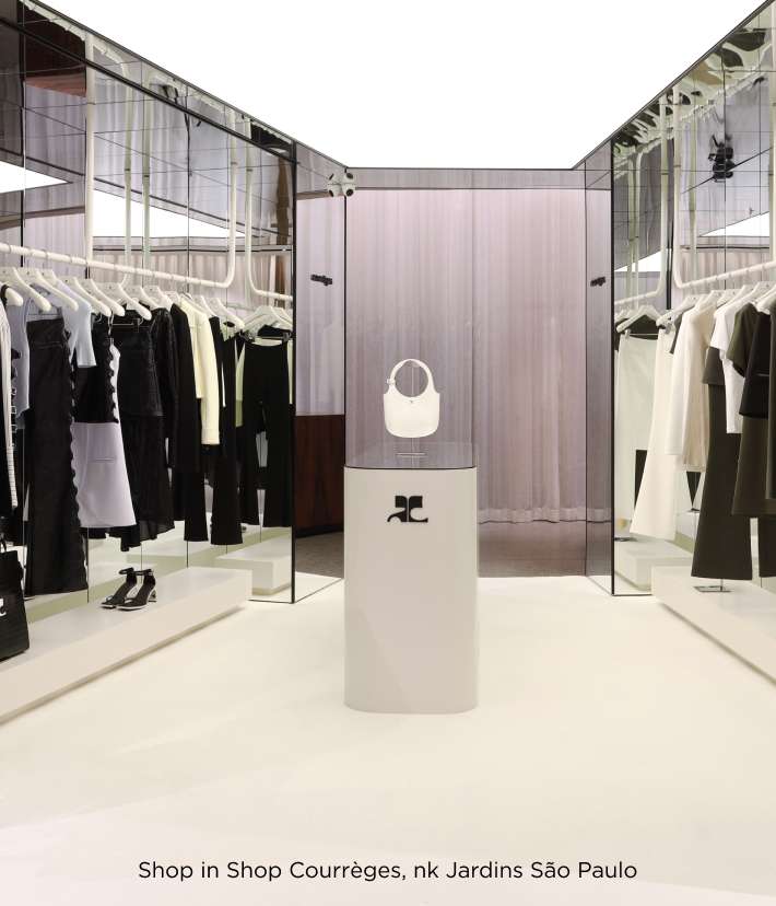 A imagem retrata uma boutique da marca Courrèges com design minimalista, apresentando uma coleção elegante em tons de preto, branco e verde militar. Os manequins exibem peças de vestuário contemporâneas penduradas em cabides brancos, dispostos em um ambiente ampliado por espelhos e iluminação suave. No centro, destaca-se um pedestal branco com uma bolsa circular e sapatos pretos, criando um cenário sofisticado que reflete o estilo refinado da marca. Localizada no shopping Jardins em São Paulo, a loja transmite uma estética moderna e clean, convidando os clientes a experimentar uma moda minimalista e atual.